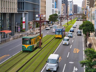 Modern binalar ve işlek caddelerle çevrili Kagoshima, Kyushu, Japonya şehir merkezindeki çimlerle kaplı bir pistte tramvaylar çalışır..