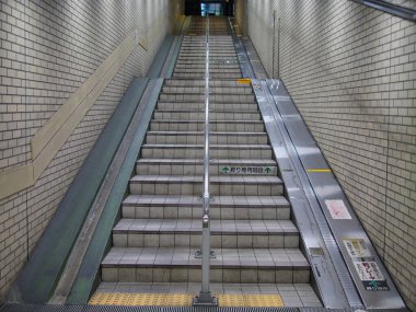 Japonya, Fukuoka 'da bir metro istasyonunda yol gösterici rayları, bisikleti ve bagaj taşıyıcısı olan merdiven. Güvenlik levhası ve fayanslı duvarları olan işlevsel şehir altyapısı.