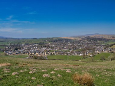 Yerleşim 'in panoramik manzarası, Yorkshire Dales' in pitoresk bir kasabası, yuvarlanan yeşil tepeler, dağınık evler ve açık mavi bir gökyüzü.