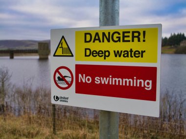 Bowland Ormanı 'ndaki Stocks Reservoir' da, derin su uyarısı ve yüzmeyi yasaklayan, içinde bir üçgen uyarı sembolü ve üzeri çizilmiş bir yüzücü de dahil olmak üzere sarı ve kırmızı bölümler içeren işaretli yüzme yasağı imzalayın. Stocks Reservoir 'daki