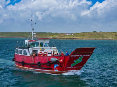 Baltimore, İrlanda - 31 Mayıs 2025: Sherkin Feribotu, yemyeşil tepeler ve dramatik bulutlarla Baltimore, İrlanda 'nın canlı mavi sularında yol alır..