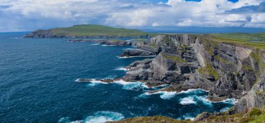 Kerry, İrlanda - Haziran 05 2025: İrlanda 'nın Kerry kentindeki çarpıcı uçurumlar, canlı bir gökyüzü altında, Atlantik' in çarpan dalgalarının üzerinde yükseliyor.