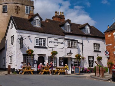 Ludlow, İngiltere - Ağustos 09 2025: Turistler, Ludlow, Shropshire, İngiltere 'de güneşli bir yaz gününde The Wheatsheaf Inn' in dışındaki piknik masalarında dinleniyorlar. Asılı sepetleri ve mavi gökyüzü olan tarihi bar cephesi.