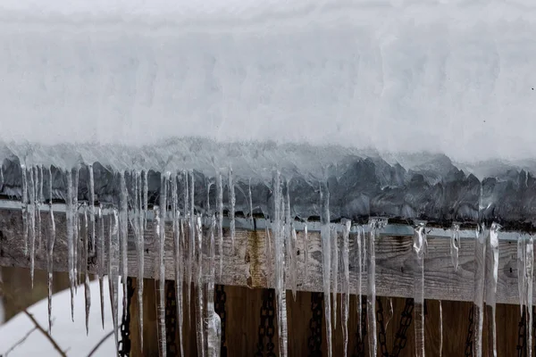 Icicles and ice dam on roof edge during winter with snow. Selective focus, background blur and foreground blur.