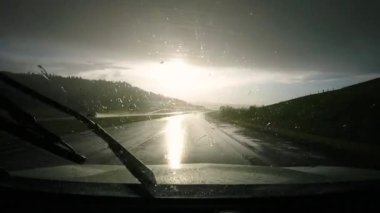 Yağmurlu bir günde, güneş ıslak yolda parlarken ve silecekleri çalıştırırken