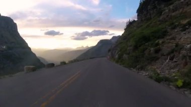 Yaz boyunca, Montana 'daki Buzul Ulusal Parkı' nda, gün batımına doğru bir kaya yüzeyi duvarının yanında araba sürerken.