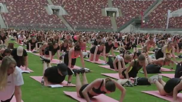 在绿色草坪的大运动场上 许多人在做伸展瑜伽运动的同时 还与老师一起进行了群众运动瑜伽活动 — 图库视频影像