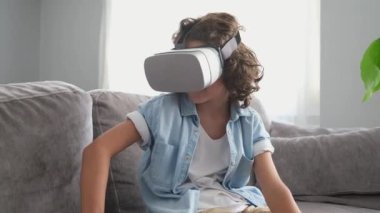 Mutlu küçük çocuk sanal gerçeklik kulaklığı takıyor evde el kol hareketi yapıyor sanal gerçeklik oyunları oynayarak eğleniyor.
