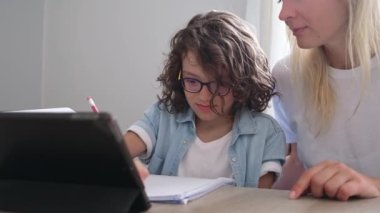 Kıvırcık saçlı ve gözlüklü anne ve küçük oğlan dizüstü bilgisayarda birlikte ders çalışıp ödev hazırlıyorlar.. 