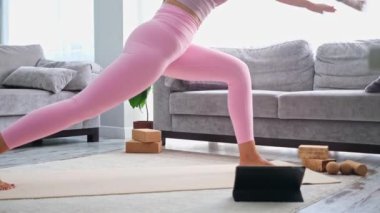 Yoga yapan kadın, evde blog öğretmeni yoga internetteki sağlık koçunda tablet dizüstü bilgisayarın önünde gerinerek poz veriyor.
