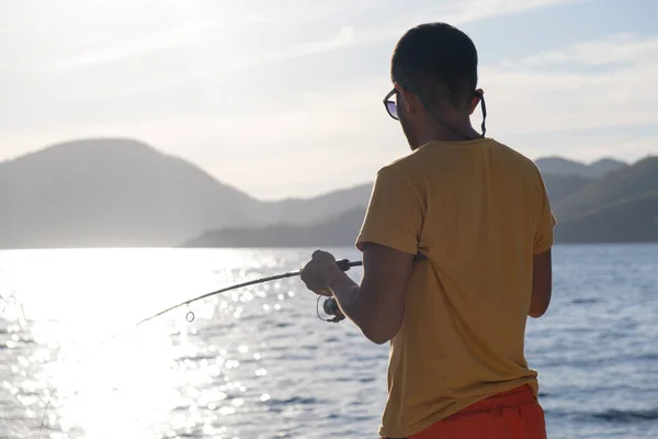 stock image Young man fishing on a lake from the boat at sunset.reflection on water