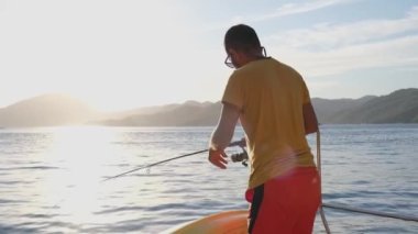 Genç adam gün batımında tekneden gölde balık tutuyor. Suya yansıyor.