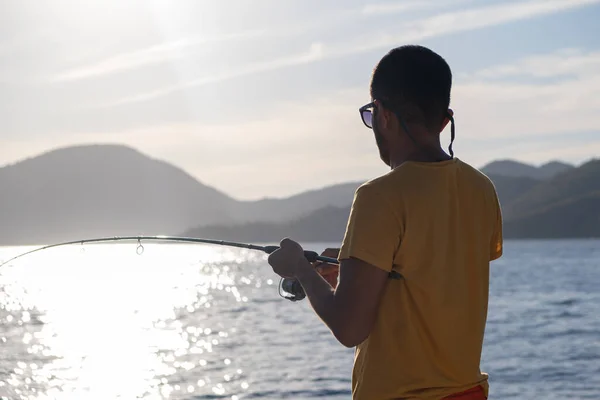 stock image Young man fishing on a lake from the boat at sunset.reflection on water