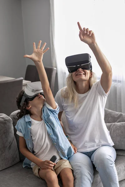 Anne ve oğlu sanal gerçeklik kulaklığı takıyor evdeki oturma odasında sanal gerçeklik oyunları oynayarak eğleniyorlar.