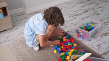 Küçük çocuk renkli plastik bloklarla oynuyor. Oturma odasında. Halı yapımı yaratıcı oyun, hayal gücü.