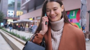 Alışveriş merkezinin dışında çantalı mutlu genç bir kadın telefonla konuşuyor. Gülümsüyor, portreyi yakından çekiyor, iş görüşmeleri yapıyor..