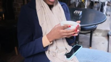 Happy African American woman sitting in cafe drinking coffee smiling thinking looking around tourist autumn coffee break cloae up