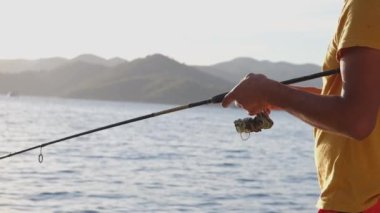 Genç adam gün batımında tekneden gölde balık tutuyor. Suya yansıyor.