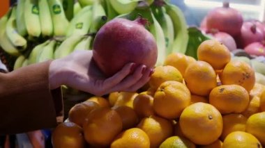 close up woman hand choosing pomegranate at fruit vegetable shelf in grocery store supermarket healthy food nutrition