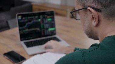 Back view of man in eye glasses analysing stock market charts on laptop. Bitcoin and crypto currency investment concept.