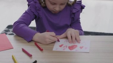 cute little girl is drawing a greeting card for her mother with red heath shape . Happy Mothers Day or womans day concept 