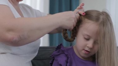 hairdresser brushing child girl blond hair and styling hairdo braid hairstyle getting ready for school or going out
