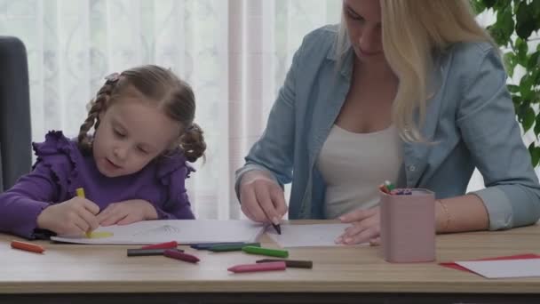 若い家族は家のリビングで一緒に自由な時間を過ごす 母と娘は紙の上にカラフルな鉛筆で絵を描く幸せな笑顔 — ストック動画