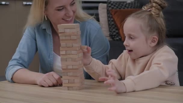 小さな娘見る興奮へJenga木製のレンガの塔 お母さん教えるかわいい女の子に遊びボードゲーム お母さんと子供過ごす時間に家で遊ぶ — ストック動画
