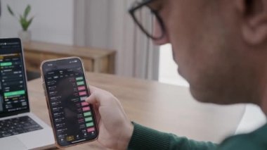 businessman in eye glasses analysing stock market charts on laptop and smartphone screen. Bitcoin and crypto currency investment concept.