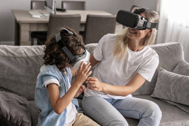 Anne ve oğlu sanal gerçeklik kulaklığı takıyor evdeki oturma odasında sanal gerçeklik oyunları oynayarak eğleniyorlar.