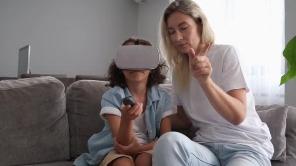 妈妈帮助儿子在家里客厅里戴虚拟实境耳机或眼镜 与虚拟实境游戏进行有趣的互动 — 图库视频影像