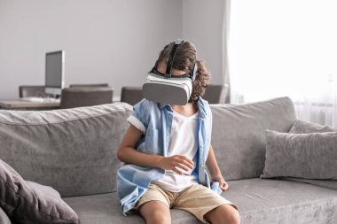 Mutlu küçük çocuk sanal gerçeklik kulaklığı takıyor evde el kol hareketi yapıyor sanal gerçeklik oyunları oynayarak eğleniyor.