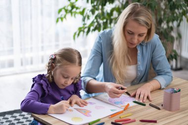 Çocuklar için yaratıcılık becerileri geliştirme hobileri. Anne ve küçük kız rahat oturma odasında, anne ve kız renkli kalemler ve pastel boyalarla resim yapıyorlar.