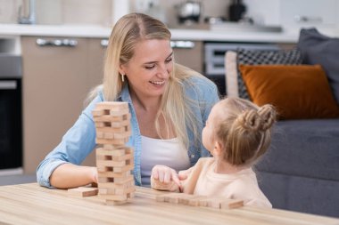 having fun with child at weekend. mother helps to kid to develop her creativity by playing board game in living room smiling cheerful