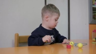 Down sendromlu şirin çocuk geometrik şekilli oyuncaklarla oynuyor. bir odada eğitim bloklarıyla öğrenme oyunu