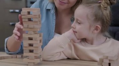 Jenga kulesine bakan mutlu küçük kız mantıklı kararlar alıyor ve annesiyle tahta masada oyun oynamaktan zevk alıyor. yavaş çekim