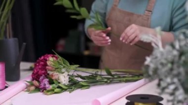 Çiçekçi dükkanındaki deneyimli çiçekçi müşterilere güvenli ve verimli bir teslimat için hazırlar ve paketler hazırlar..