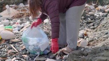 Eldivenli bir kadın, çöpleri topluyor ve halk plajındaki plastik kirlilikle savaşmak için bir çöp torbasına koyuyor. Doğayı atıklardan korumak 