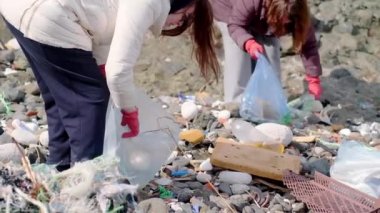 İki kadın plajda poşetlerde plastik çöp topluyor. Kirlilik felaketinin etrafına çöp döktü. Boş plastik şişeler ve kağıt atıkları