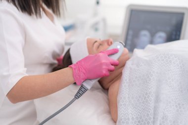 Bir kadın kuaförde, profesyonel bir güzellik uzmanı tarafından ustalıkla işletilen ultrasonik bir aletle cerrahi olmayan bir yüz gerdirme ameliyatı oluyor..