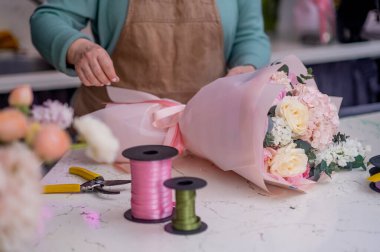 Çiçek tasarım stüdyosunda çiçekçi kadın. İnternetten siparişler için gül buketleri hazırlıyor..