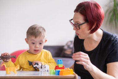 Down sendromlu şirin bir çocuk evde oyuncaklarla oynuyor ve komik yüz ifadeleri sergiliyor, yeni oyunlar keşfediyor.