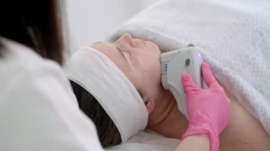Kadın kozmetik uzmanı ultrasonla yüz gerdirme güzellik tedavisi uyguluyor. Müşteri, bir kuaför salonunda rahat bir şekilde yatarken bir profesyonel de ihtiyaçlarını karşılıyor..
