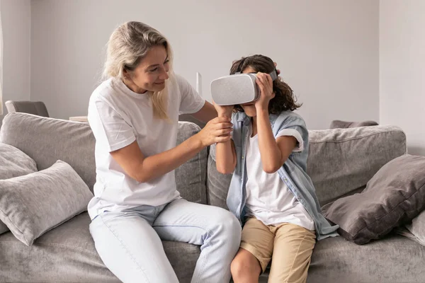 Mother helping his son to wear virtual reality headset vr glasses in living room at home having fun interracting with virtual reality playing games
