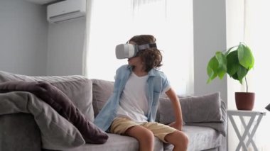 Mutlu küçük çocuk sanal gerçeklik kulaklığı takıyor evde el kol hareketi yapıyor sanal gerçeklik oyunları oynayarak eğleniyor.