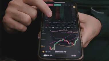 close up smartphone with stock market graph on touch screen with hands scrolling, checking stock market data, selective focus. 
