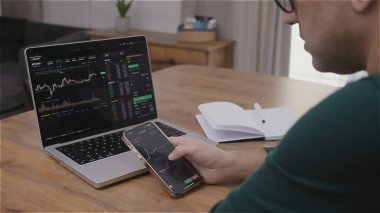 Genç finansal analist, bilgisayar ve akıllı telefon kullanarak borsada kripto alıp satıyor. Yatırım aracılığı ticaret kavramı.