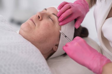 Güzel, orta yaşlı, olgun bir kadın kozmetik kullanıyor. Yaş karşıtı enjeksiyonlar, cilt estetiği, kozmetoloji konsepti. 