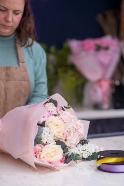 Modern ve zarif çiçekçi, yetenekli çiçekçi yardımcısı çeşitli ve renkli çiçeklerden bir buket hazırlar ve yaratır.