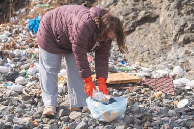 Plajdaki plastik atıkları temizleyen, sürdürülebilirliği ve korunmayı destekleyen bir kadın. Çöp geri dönüşümü ve çevresel bakım kavramı